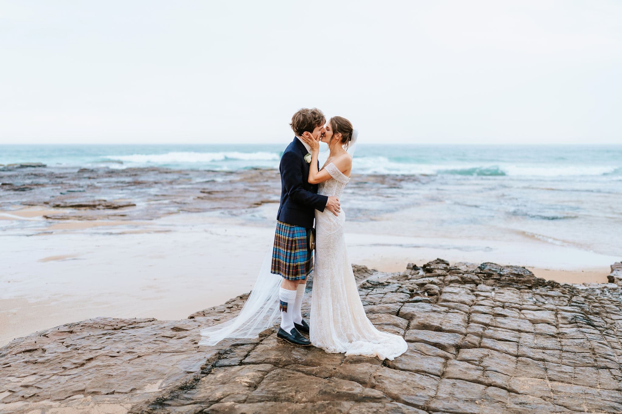 Mandy and Marcus kissing beside the ocean on their wedding day