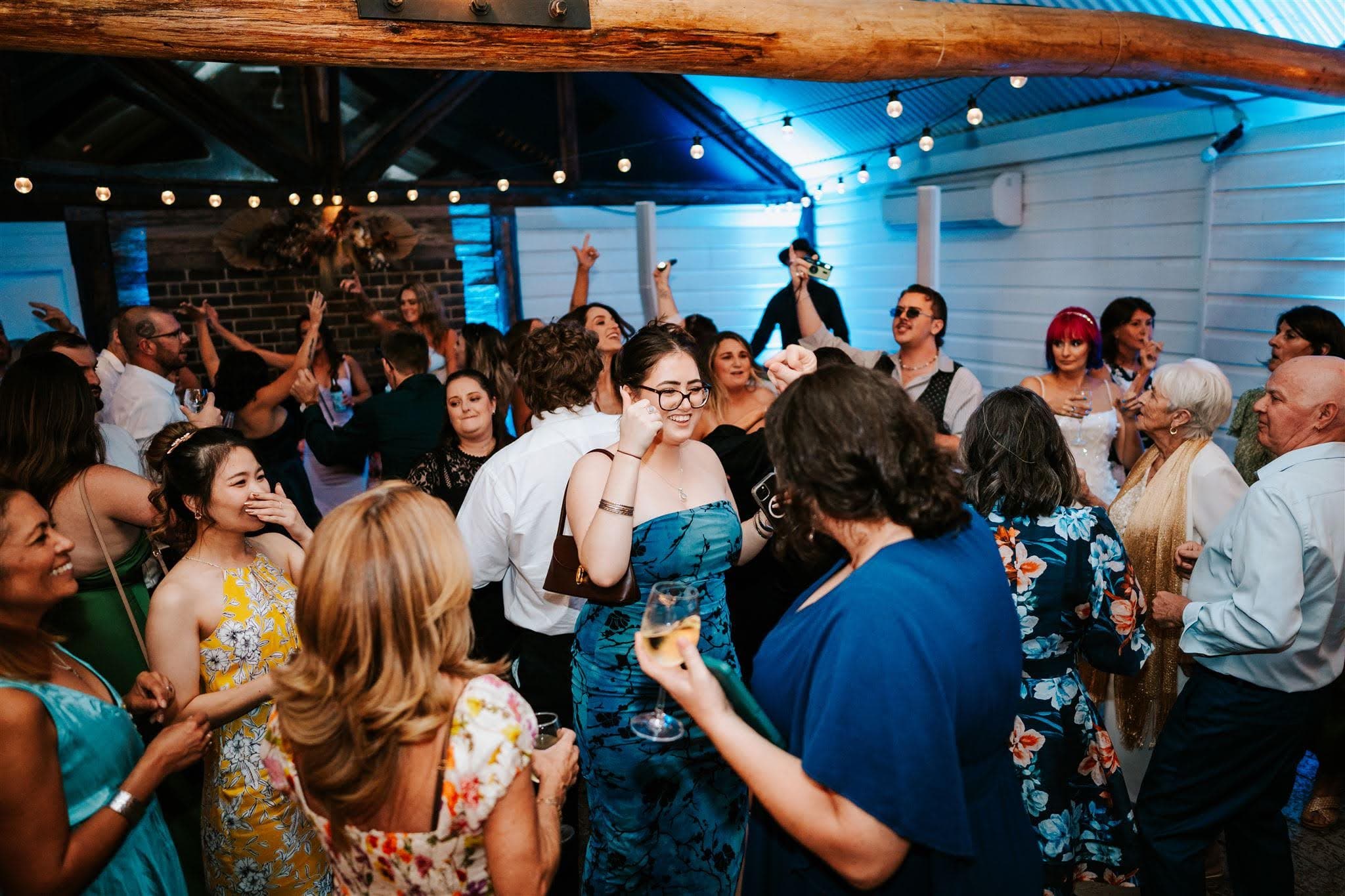 Wedding guests dancing together beneath timber beams and festoon lights at Robertson Public House