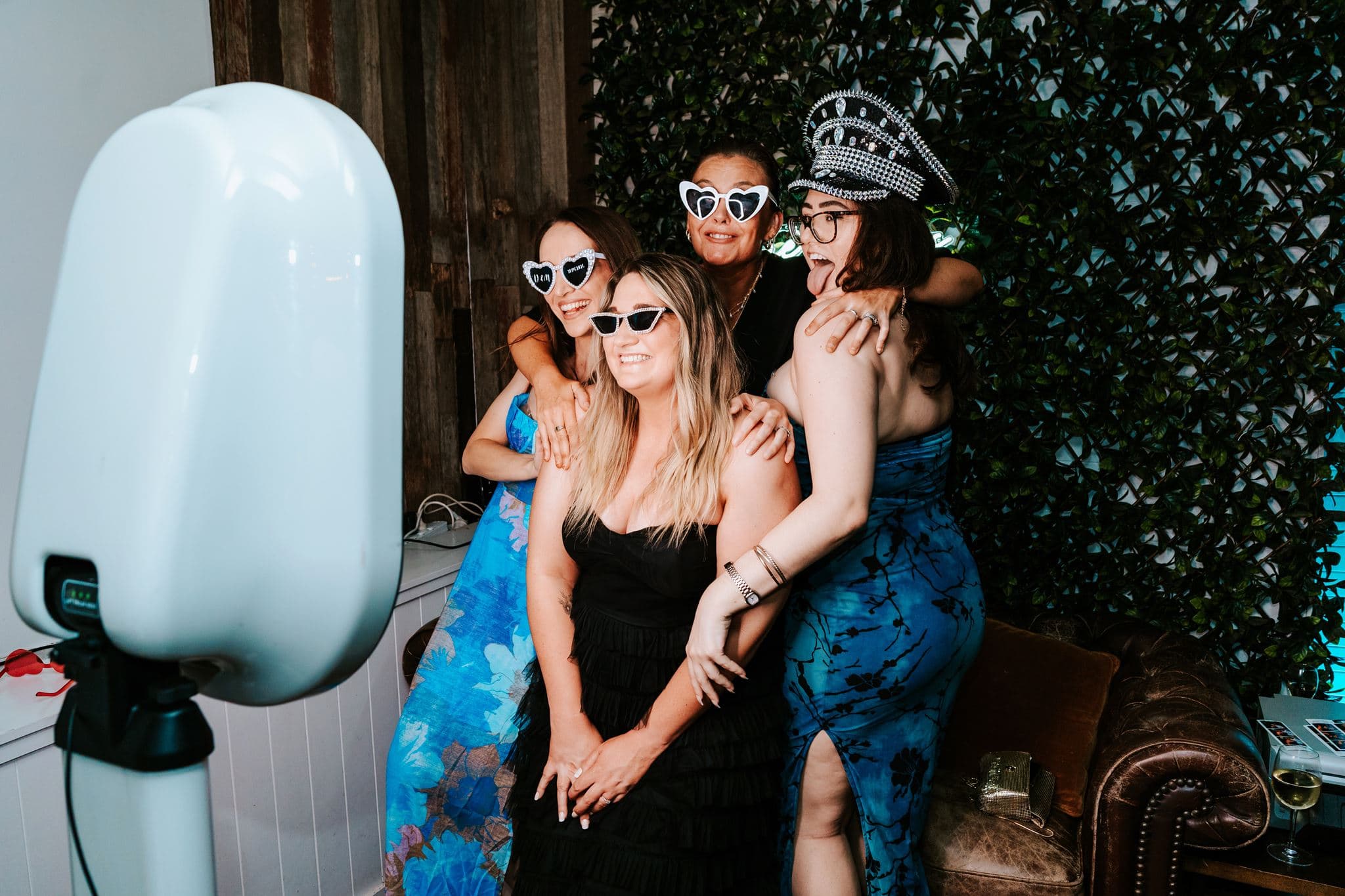 Friends wearing heart-shaped sunglasses and a sparkly hat as they pose together at Matt and Dom’s photobooth