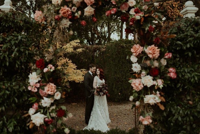 Cailin and Brandon framed by flowers in the gardens at Jaspers Berry