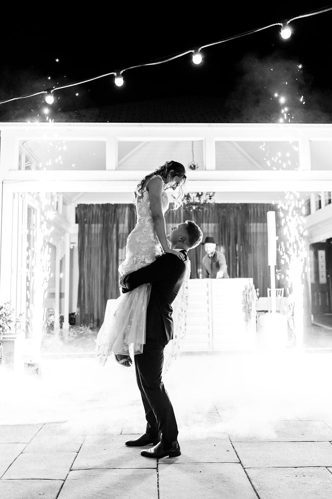 William lifting Mikayla during their first dance, framed by spark fountains